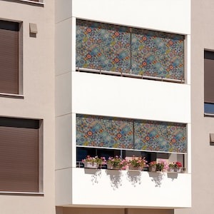 Puede incluir: Un edificio con persianas metálicas marrones y un balcón con cortinas de ventana estampadas y plantas en macetas.