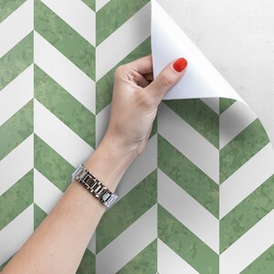 May include: A roll of green and white chevron patterned wallpaper being peeled back to reveal the adhesive backing.