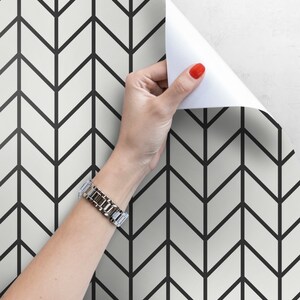 May include: Black and white chevron patterned wallpaper with a hand peeling back a corner to reveal the pattern.