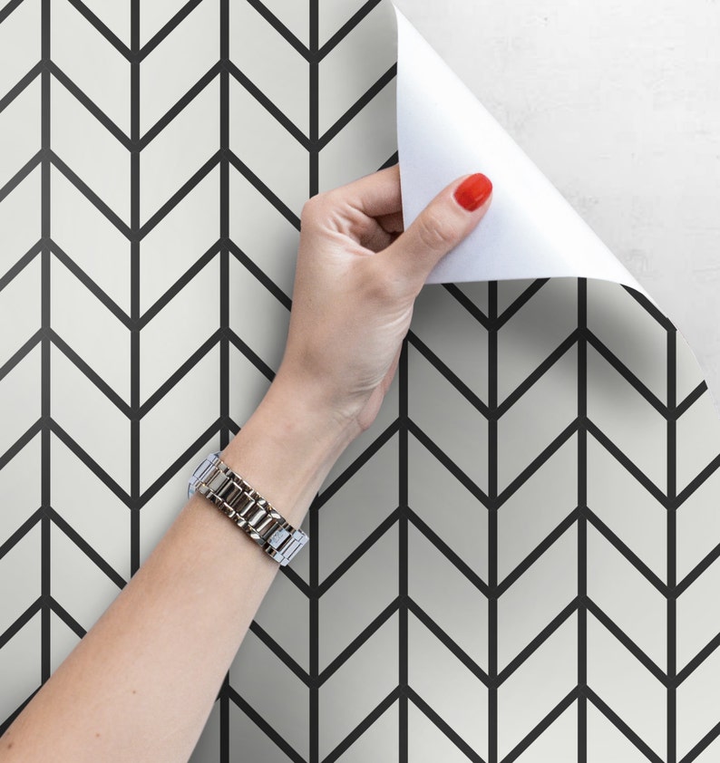 May include: Black and white chevron patterned wallpaper with a hand peeling back a corner to reveal the pattern.