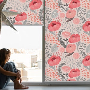 Peut inclure: Une fenêtre avec un store enrouleur à motif floral. Le store présente des fleurs roses et des feuilles grises sur un fond rose clair. Une jeune personne est assise sur le rebord de la fenêtre.