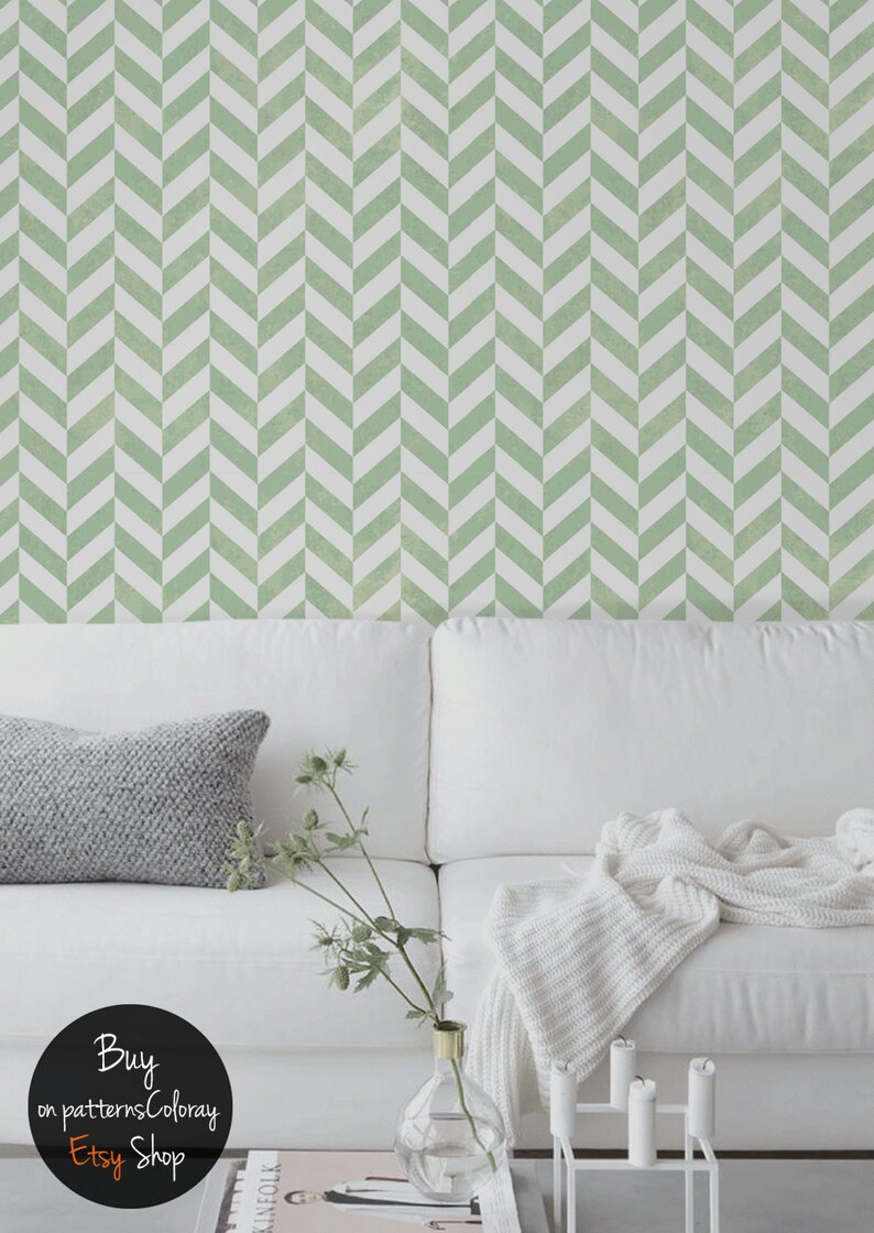 May include: A white sofa with a gray throw pillow and a white blanket. The wall behind the sofa is covered in a green and white chevron patterned wallpaper. A vase with green stems and a glass vase with a gold top are on a coffee table in front of the sofa.