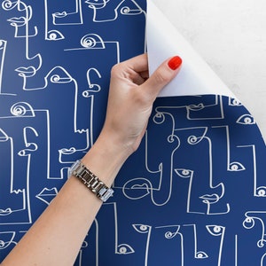 May include: A roll of blue wallpaper with a white line drawing pattern of abstract faces. The wallpaper is being peeled back to reveal the white backing.