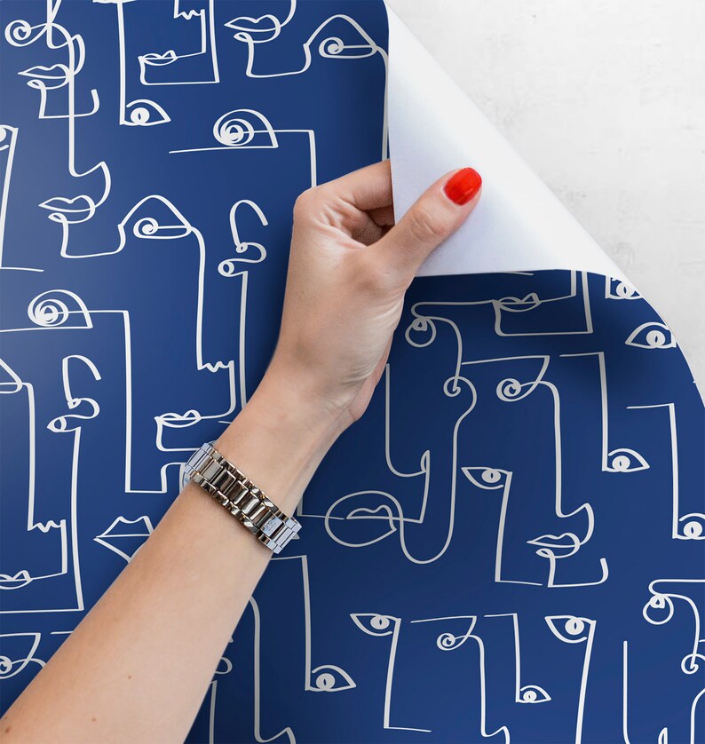 May include: A roll of blue wallpaper with a white line drawing pattern of abstract faces. The wallpaper is being peeled back to reveal the white backing.