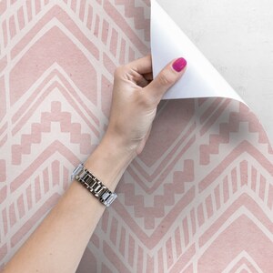 May include: Pink and white geometric patterned wallpaper with a hand peeling back a corner to reveal the white backing.