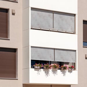 May include: A modern building with multiple windows featuring brown roller shades. The windows are on a beige wall. The building has a white balcony with a gray awning and potted plants.