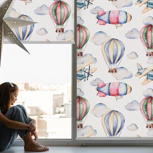 Peut inclure: Un store de fenêtre avec un motif aquarelle représentant des montgolfières, des avions et des nuages. Le motif est dans des tons de bleu, vert, rouge et jaune.