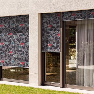 May include: Two windows with black and white geometric patterned shades. The shades are pulled down and the windows are closed. The windows are framed in brown.