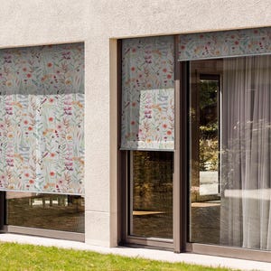 May include: Two windows with floral patterned roller shades. The shades are partially rolled up, revealing a view of a green lawn outside the windows.