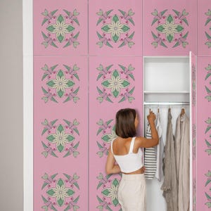May include: Pink wardrobe with a floral pattern in green, cream, and pink. The wardrobe doors are closed, except for one that is open, revealing clothes hanging inside. A person is reaching into the open wardrobe.
