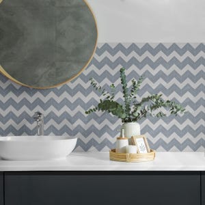 Puede incluir: Un tocador de baño con un lavabo de cerámica blanca y un espejo redondo. El salpicadero es de azulejos de chevron azul y blanco. Una bandeja pequeña con un dispensador de jabón, una vela y un marco de fotos se encuentra en el mostrador.