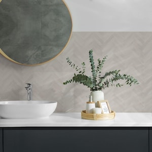 Op de afbeelding: Een moderne badkamer met een wit aanrecht, een witte ovale wastafel en een donkergrijze kast. Boven de wastafel hangt een ronde spiegel met een gouden lijst. Een gevlochten dienblad bevat een zeepdispenser, zeep en een ingelijste foto.