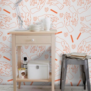 Pu&ograve; includere: Un tavolino bianco con un cassetto e due ripiani. Il tavolino &egrave; decorato con una tazza in ceramica bianca, un set di piatti bianchi, una bottiglia di vetro trasparente, una scatola bianca e un contenitore giallo. Il tavolino &egrave; davanti a un muro bianco con un motivo ripetitivo di disegni di mani arancioni.