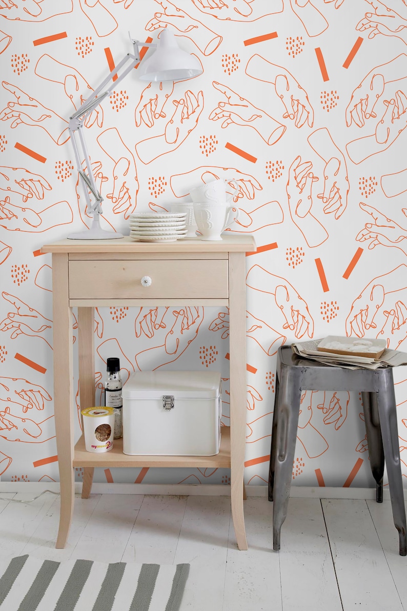 Pu&ograve; includere: Un tavolino bianco con un cassetto e due ripiani. Il tavolino &egrave; decorato con una tazza in ceramica bianca, un set di piatti bianchi, una bottiglia di vetro trasparente, una scatola bianca e un contenitore giallo. Il tavolino &egrave; davanti a un muro bianco con un motivo ripetitivo di disegni di mani arancioni.
