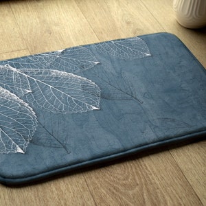 May include: A blue bath mat with a white leaf design. The mat has a textured surface and a white border.
