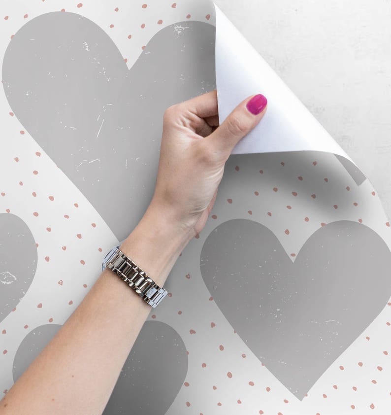 May include: A white background with a repeating pattern of gray hearts and small pink dots. A hand is peeling back a corner of the wallpaper to reveal the pattern.