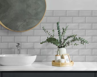 May include: White subway tile bathroom with a round mirror, a white porcelain sink, and a wooden tray with a vase of eucalyptus, a bottle of soap, and a small picture frame.