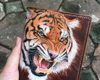 May include: A brown leather wallet with a hand-painted image of a tiger with an open mouth and sharp teeth. The tiger's fur is orange and black with white stripes.
