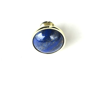 May include: A round, blue lapis lazuli gemstone set in a gold-toned metal frame. The gemstone has a swirling pattern of blue and gold.