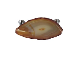 May include: A cabinet pull featuring a polished, natural agate slice in shades of brown and cream. The agate is mounted on two silver-toned metal posts for installation. This decorative hardware adds a touch of natural elegance.
