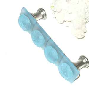 May include: A light blue glass cabinet pull with four sand dollar designs and silver metal hardware.