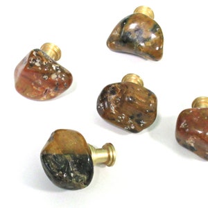 May include: Five brown, orange, and black agate stone cabinet knobs with gold metal bases.