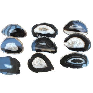 May include: A set of eight agate slices, each with a unique pattern of black and white bands. The slices are smooth and polished, and they have a natural, organic shape.