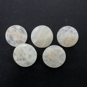 Pu&ograve; includere: Cinque cabochon rotondi, lisci, lucidi, in pietra naturale di colore bianco. I cabochon sono traslucidi, di un bianco lattiginoso con sottili inclusioni marrone chiaro.