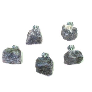 May include: Five gray rock-shaped bottle stoppers with silver-colored tops are arranged against a white background. The stoppers have a rough, textured appearance, and the metal tops are cylindrical.