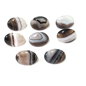 May include: Eight oval-shaped agate stones with black, white, and brown banding. The stones are smooth and polished.