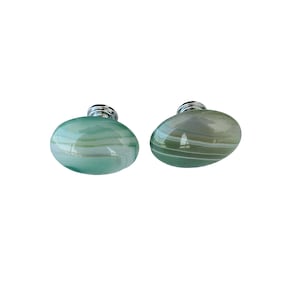May include: Two oval-shaped cabinet knobs with a polished, striped stone appearance. One is a light teal color, and the other is a muted green. Each knob has a silver-colored metal base.