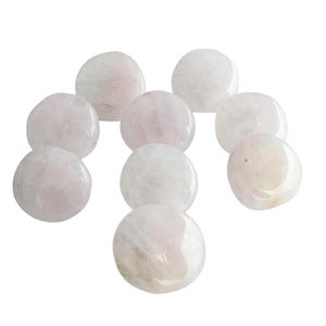 May include: A collection of eight smooth, polished, round stones in a pale, translucent pink hue. Each stone features a glossy surface with subtle internal variations and cloudy white inclusions, arranged in a loose, scattered cluster formation.