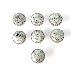 May include: Seven round cabinet knobs with a speckled, light green and gray design. Each knob has a silver-colored metal rim. The knobs are arranged in a pattern on a white background, suitable for furniture or home decor.