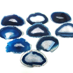 May include: Set of eight blue agate coasters with white crystal formations in the center. The coasters are irregularly shaped and have a natural, polished finish.