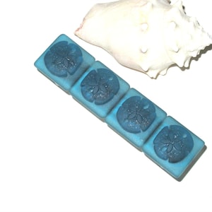 May include: Four square blue glass tiles with a sand dollar design. The tiles are arranged in a row.