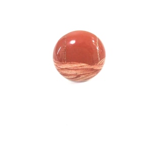 May include: A round, red and white stone with a swirling pattern. The stone is smooth and polished.