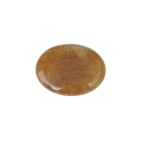 May include: An oval-shaped, amber-colored gemstone with a textured surface. The stone has a polished, glossy finish and is set against a white background. The gemstone's color ranges from light to dark brown.
