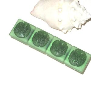 May include: Four green glass tiles with a sand dollar design. The tiles are arranged in a row.