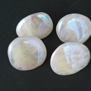 May include: Four iridescent, oval-shaped stones with a pearlescent sheen. The stones are a pale yellow color and reflect a rainbow of colors. The stones are arranged in a square on a black surface.