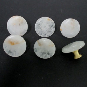 Pu&ograve; includere: Sei pomelli per armadi rotondi in cristallo bianco con accenti dorati. Un pomello ha una base in metallo dorato e una parte superiore rotonda in cristallo.