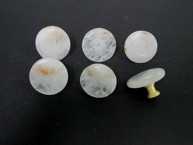 Pu&ograve; includere: Sei pomelli per armadi rotondi in cristallo bianco con accenti dorati. Un pomello ha una base in metallo dorato e una parte superiore rotonda in cristallo.