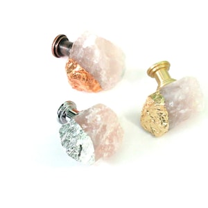 May include: Three pink quartz drawer pulls with gold accents. The pulls have a rough, natural look and are attached to a metal base.