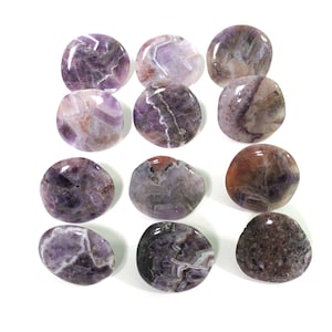 May include: An overhead shot displays twelve polished amethyst stones. The stones are oval-shaped, with a mix of purple, white, and brown hues. Each stone has a unique pattern and a glossy finish, set against a white background.