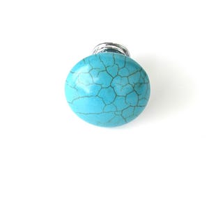 May include: A round, turquoise cabinet knob with a silver base. The knob has a cracked, marbled appearance, and is set against a white background. This decorative hardware is suitable for drawers and cabinets.
