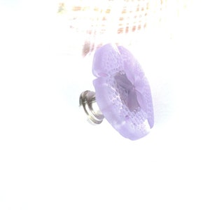 May include: A lavender glass flower knob with a silver base. The knob has a textured surface and a hole in the center.