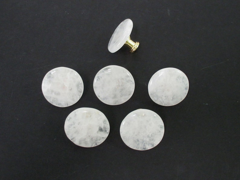 Pu&ograve; includere: Sei pomelli rotondi in quarzo bianco con una vite in metallo dorato su un pomello.