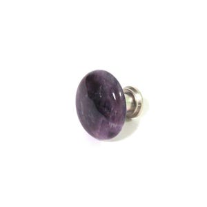 May include: A single, oval-shaped amethyst stone knob with a silver-colored metal base. The polished purple stone has natural variations in color and texture. The knob is set against a white background.
