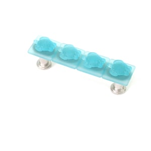 May include: A light blue glass cabinet knob with four frosted glass squares, each with a raised design. The knob has a silver metal base.