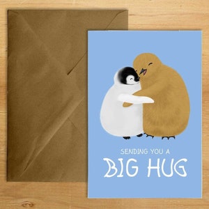 Könnte beinhalten: Grußkarte mit hellblauem Hintergrund, die eine Illustration von zwei Pinguinen zeigt, die sich umarmen. Der Text "SENDING YOU A BIG HUG" ist in Weiß geschrieben. Ein brauner Umschlag befindet sich links.