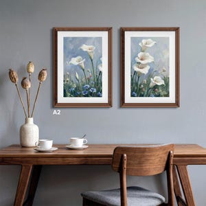 Set of two A2 wood frames hanging side-by-side on a gray wall above a wooden desk. Each solid birch wood picture frame features custom white matting displaying elegant floral artwork. A perfect hanging photo frame solution for creating a stylish gallery wall or elevating your home office and living room decor.